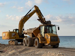 CAT excavator loading an articulated dump truck on the beach